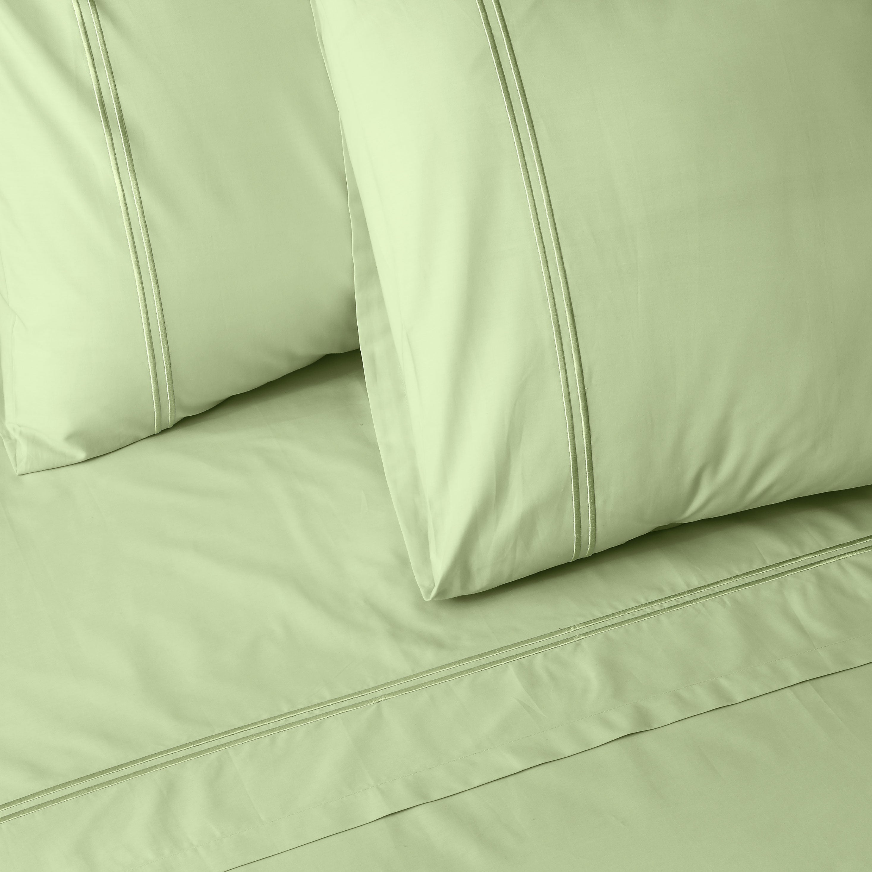 Close-up of light green colour luxury embroidered bedding with two pillows on a matching bed sheet.