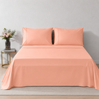A neatly made bed with peach-colored 250TC organic cotton sheet and two matching pillowcases, styled in a minimalist bedroom setting with a small side table and flowers.