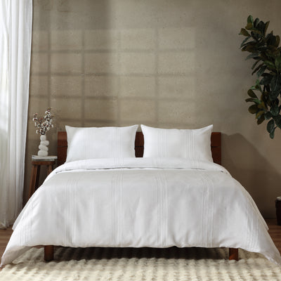 Full bed with Heirloom Whisper White pure linen duvet cover set, wooden headboard, and plant against concrete wall. European French Flax