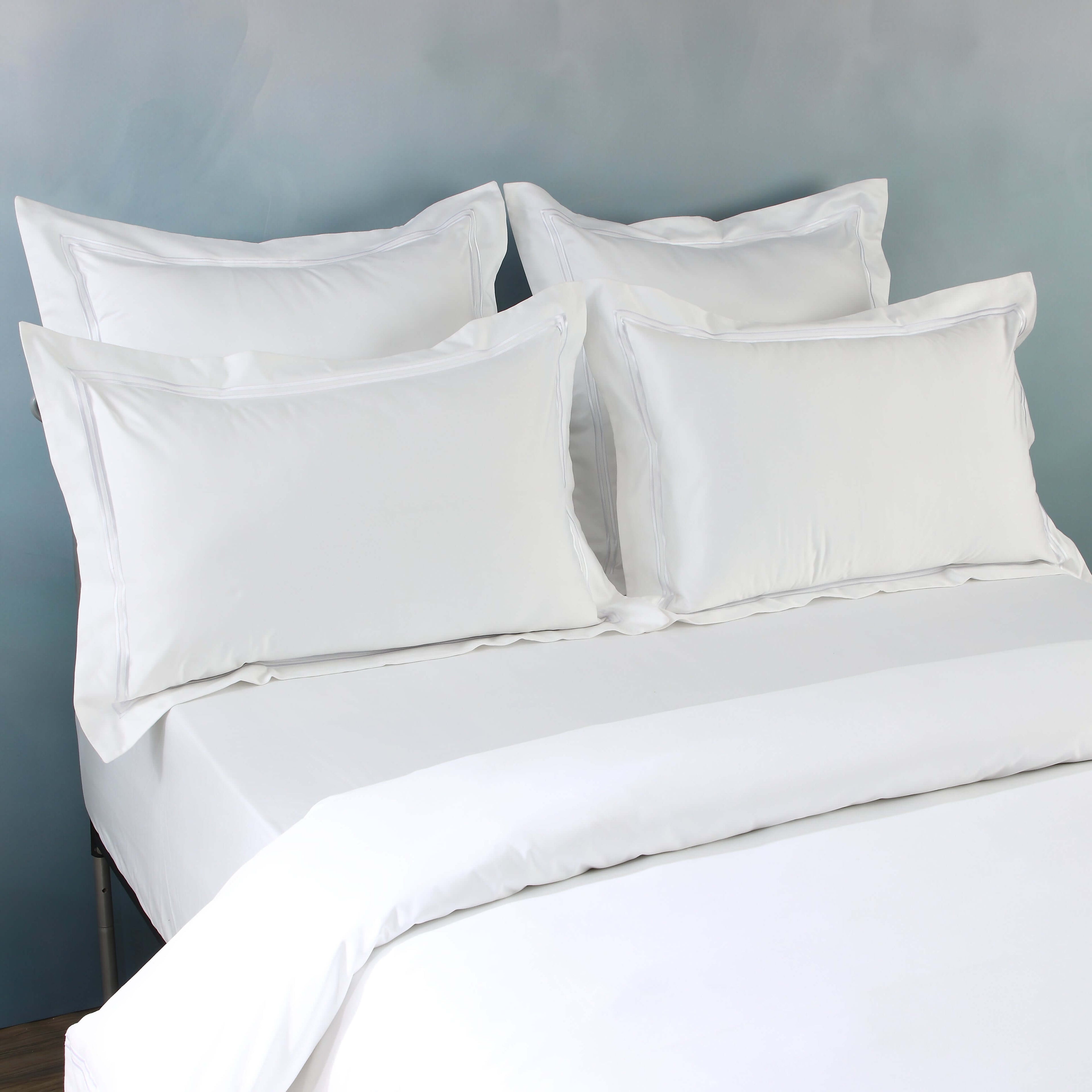 Multiple white oxford pillowcases layered on bed, part of 1250TC GOTS certified organic cotton pillowcases
