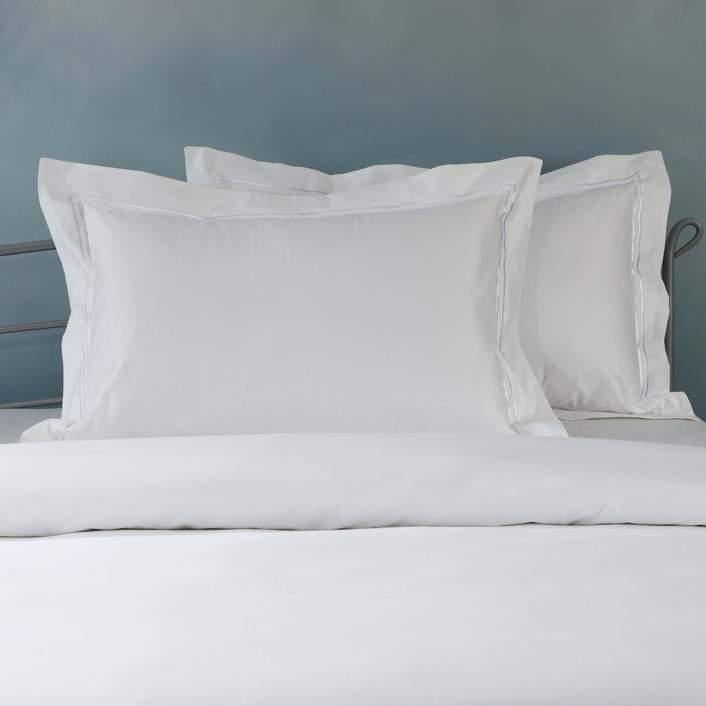 Close-up of 1250TC organic cotton pillowcases in white with oxford style and embroidered detail on styled bed