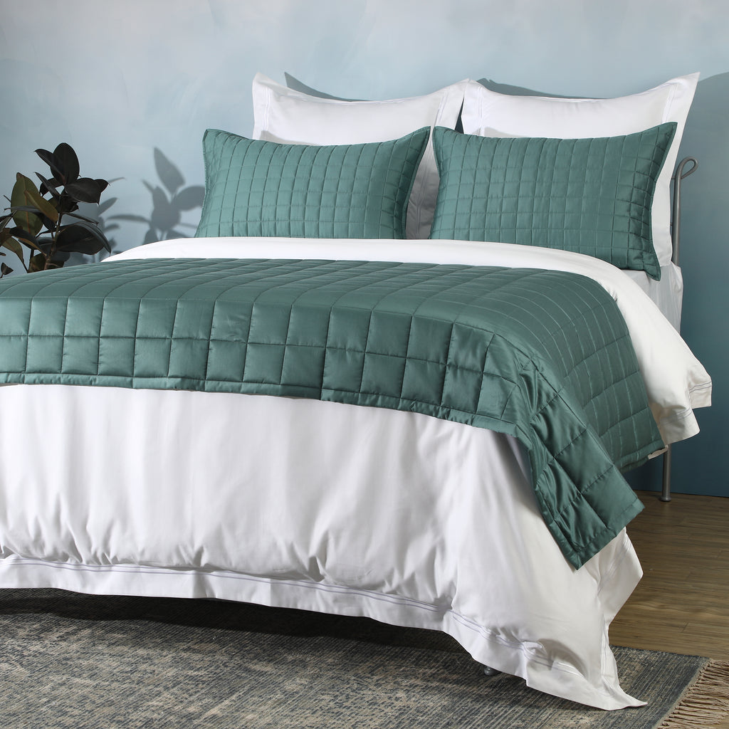 Angled shot of teal bedspread over white duvet with pillowcases: Teal bamboo cotton bedspread set quilted square design layered white duvet Whites of London