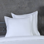 Two white euro pillowcases propped against metal headboard, part of 750TC GOTS certified organic cotton pillowcases