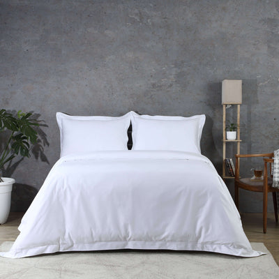 Full bed front view of 750TC GOTS certified organic cotton duvet cover set in white with matching pillowcases on styled bed featuring concrete wall, plant, and shelf, Whites of London 