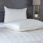 Two ivory pillowcases from Bamboo Cotton Bedspread Set stacked on bed showing quilted square stitching detail, styled with concrete wall and shelf, Whites of London NZ 